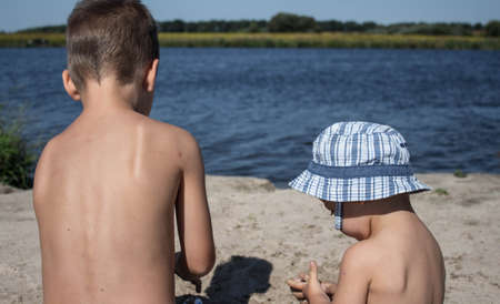 a brother with younger sister play with sand near the riverの写真素材