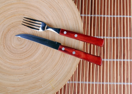 wooden round dish and red cutlery on bambooの写真素材