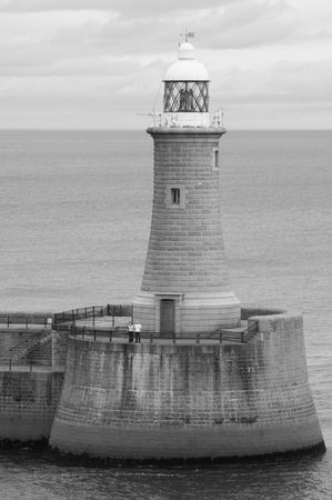 A shot of a lighthouse taken when sailing out of the Newcastle harbor. The horizon lines up perfectly with the roof of the house. A couple is standing at the base.の写真素材