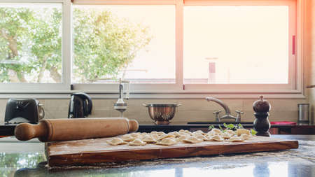 Large and illuminated kitchen where there is a homemade raw pasta and a rolling pin on the counter. The kitchen has a large window, through which a beautiful light enters. Homey warmth concept.の写真素材