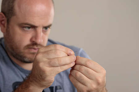 Close-up detail of man threading a sewing needle with thread. Selective focus on hands. Copy space. Concept of emancipated man.の写真素材