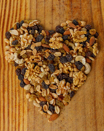 A top view of raisins with different dried fruits forming a heart on a bank background. Almonds, walnuts, hazelnuts, candied fruit, peanuts.の写真素材