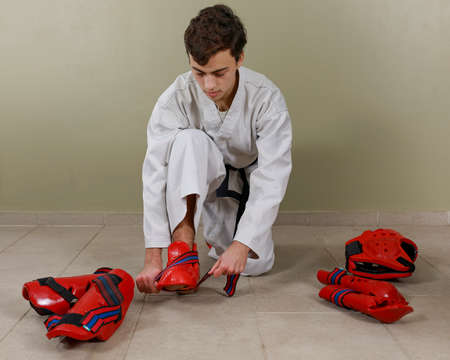 A Young Caucasian man putting on a taekwondo combat shin guard on his leg. Sportswear.の写真素材
