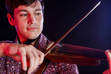 A Overhead shot of young man playing music on violin, sitting on the floor. Looking at camera....