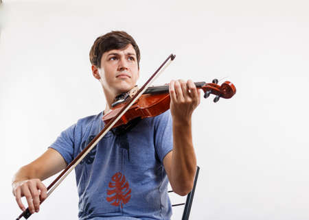 A Overhead shot of young man playing music on violin, sitting on the floor. Looking at camera. Wooden background.の写真素材