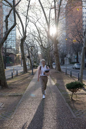 General shot and front view. Young female student with books and folders, walking down the street....
