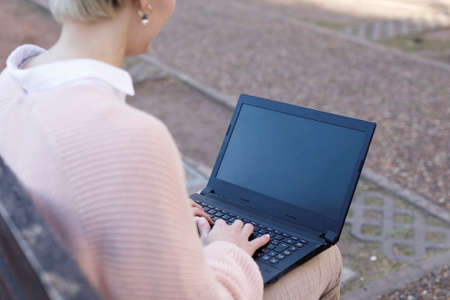 Young student or businesswoman, typing on a computer, sitting on a city street bench. Studying or...