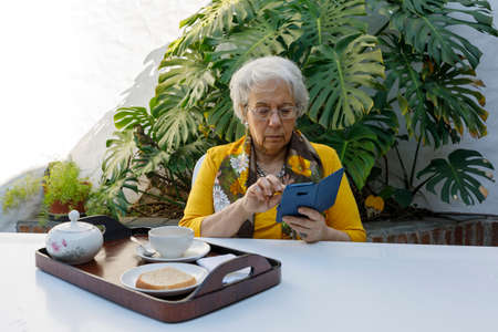 Grandmother eating breakfast while looking at smart phone.の写真素材