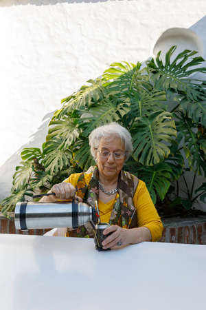 elderly woman drinking mate in the courtyard. Elegantly dressed. Outside, day. Latin American culture and customs.の写真素材