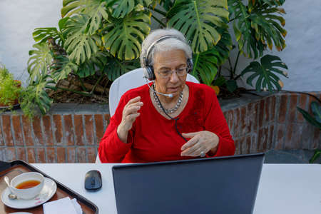A Elegant elderly lady, reading a book in the courtyard of her house, while having breakfast. Concept of wellness, prevention of Alzheimer's and other neurodegenerative diseases.の写真素材