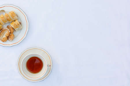 Top view of a cup of tea and sweet puff pastry dough, palms and cannons filled with dulce de leche,...