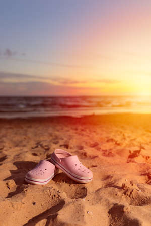 Beach slippers on the sand at sunset. Summer vacation concept. Sun reflections. Vertical image. Copy space for text.の写真素材
