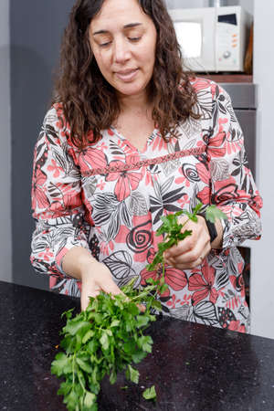Housewife with a parsley plant in her hand, in the kitchen of her home. Fresh ingredients for the preparation of a healthy meal.の写真素材