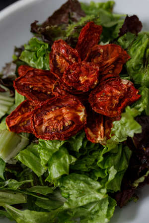 Vertical image. Close-up of white platter with variety salad of lettuce, spinach, arugula and sun-dried tomatoes.の写真素材