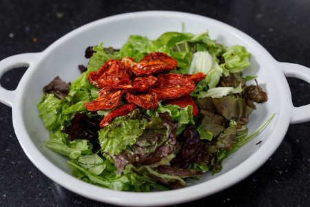 Horizontal image of white platter with salad of variety of lettuce, spinach, arugula, dehydrated tomatoes.の写真素材
