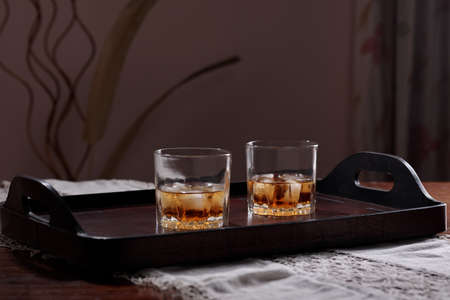 two glasses of whiskey on the rocks on a leather tray on a table. Blurred background with copy space for text.の写真素材