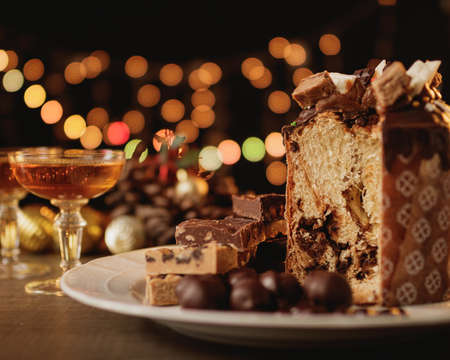 Christmas background with copy space for text and design. Christmas bread, sweets, chocolates, nougat, champagne glass, Christmas decorations and lights out of focus.の写真素材