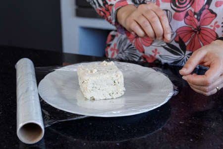 close-up of a womans hands wrapping soy cheese in kitchen stretch film. Food preservation.