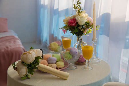 cupcakes of different colors in a pink plate next to a lush bouquet of flowers two glasses of yellow juice on the tableの写真素材