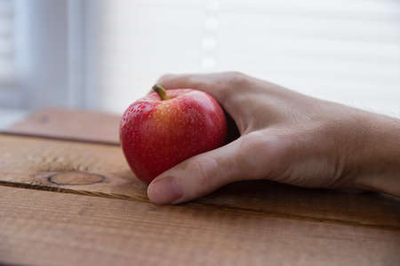 vitiligo hand holds a red apple in the palm of your hand on a wooden boardの写真素材