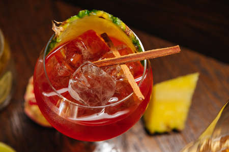 Glass of ice cold  cocktail served in a wine glass with pineapple and garnet, placed on a table in...