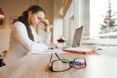 Black-rimmed glasses lie on table against background of girl with headacheの写真素材