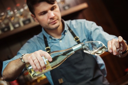 Male sommelier pouring white wine into long-stemmed wineglasses.の写真素材