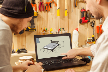 Two men looking at sketch of wooden bed on laptopの写真素材