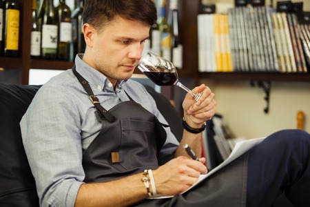 Male sommelier tasting red wine and making notes. Profession in winemaking.の写真素材