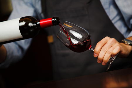 Man pouring wine into wineglass, male hand holding bottleの写真素材