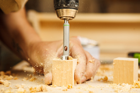 Wood boring drill in mans hand drilling hole in wooden bar, electric instrument works with wooden surfaces, equipment for construction different materials necessary in carpentryの写真素材