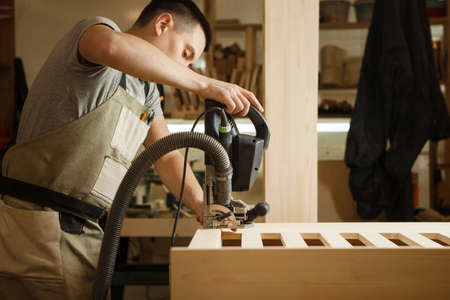 Man working with carving equipment in workshop. Electronic device makes chinseling groove in wooden...