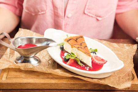 Girl eats cheesecake dessert with mint on plate, sauce bowl with strawberry jam stands on table. Woman going to eat sweet piece of cake in restaurant, closeup view on dish and ladies handsの写真素材