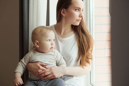 Woman and her adorable baby looking out from the window
