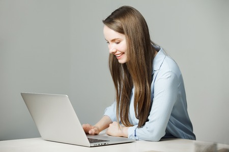 Girl in classic shirt sits at laptop and smileの写真素材