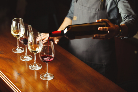 Bartender pours red wine in glasses on wooden bar counterの写真素材