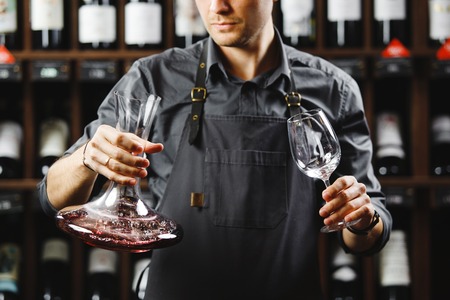 Barman in apron holds vessel with red wine and glassの写真素材