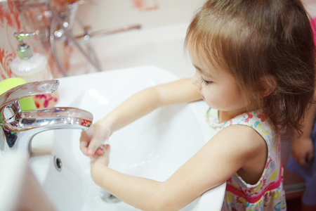 Kid wearing t-shirt washing hands in bathroom with soapの写真素材