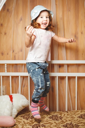 red-haired girl in a blue hat jumping on the bed.の写真素材