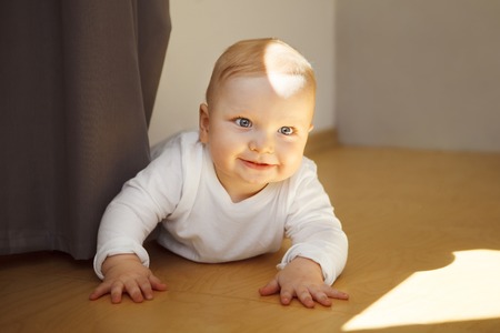 Baby with big eyes in crawlers lies on wooden floorの写真素材