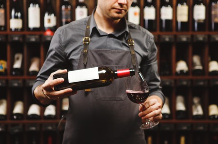 Male sommelier pouring red wine into long-stemmed wineglasses.の写真素材