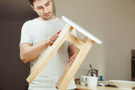 Man holding in hands wooden stool, carefully examining seat trying to find whats wrong in chair....