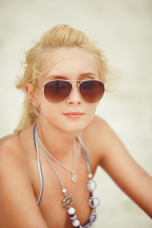 young woman with blond hair sits in a bikini on the beach. portrait of beautiful girl in a swimsuit.の写真素材