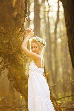 blond woman stands in white dress by tree.の写真素材