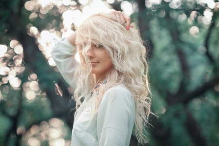 woman holds hands hair. portrait of beautiful blonde girl on the background of sunset and trees.の写真素材