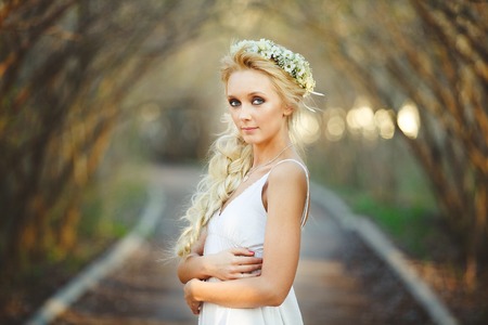 beautiful blond woman in white dress and floral wreath on her head. cute person in alley.の写真素材