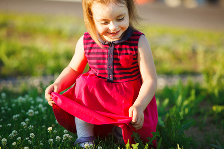 cute girl sits on a green field and holds her dress.の写真素材