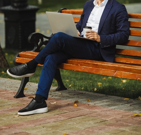 Man sitting on bench with laptop and holds coffee in hand