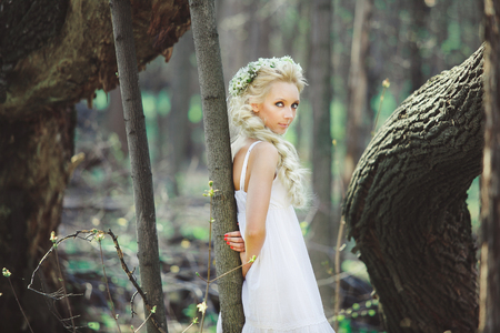 young woman with blond hair in white dress forest among trees.の写真素材