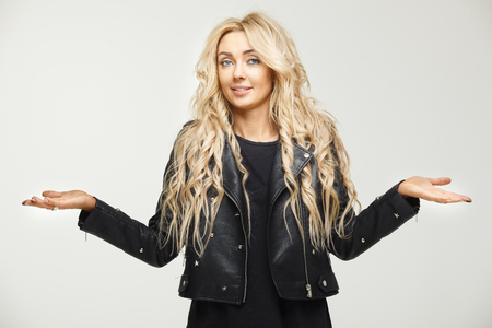 puzzled female horizontal portrait of a blonde with long hair lifting shoulders as a sign of ignorance or annoyance. Ignorance, confusion, misunderstanding and lack of knowledge.の写真素材